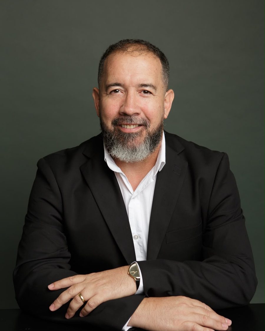 Gustavo Mateus, de terno escuro, sorrindo, com os braços apoiados sobre a mesa